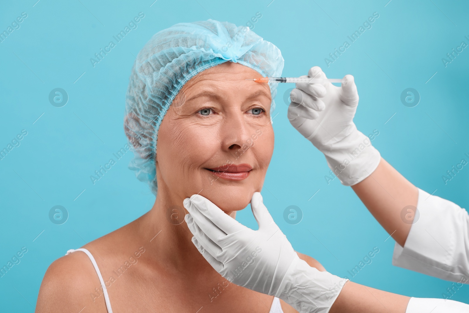 Photo of Doctor giving facial injection to senior woman on light blue background. Cosmetic surgery