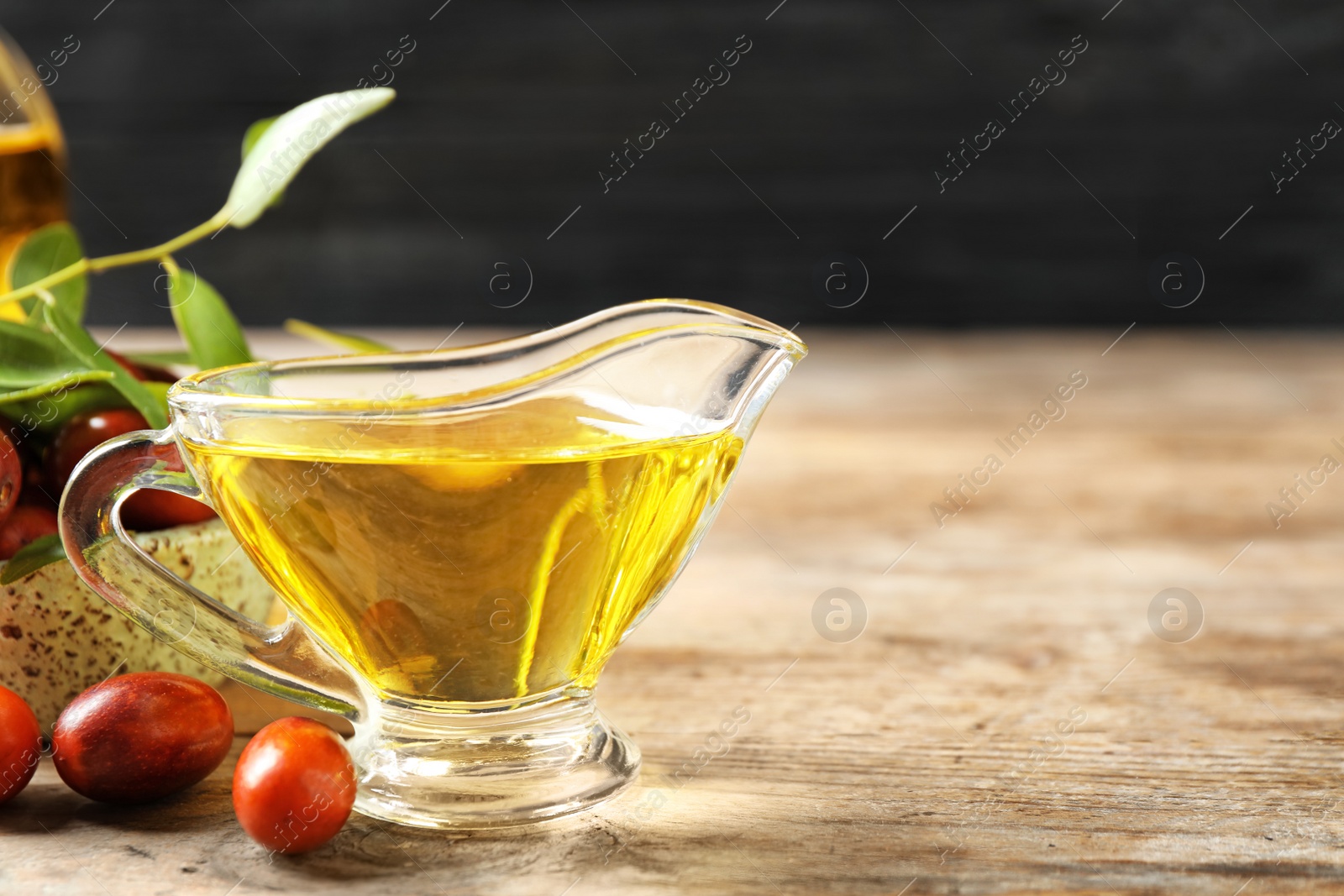 Photo of Glass sauce boat with jojoba oil and seeds on wooden table. Space for text