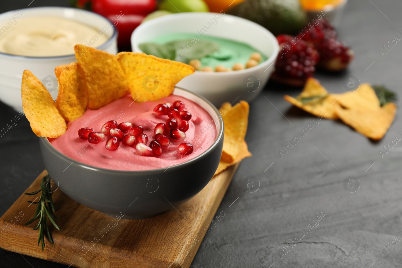 Photo of Different kinds of tasty hummus served with nachos on black table, space for text