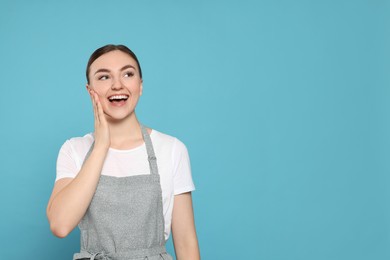 Photo of Beautiful young woman in clean apron with pattern on light blue background. Space for text