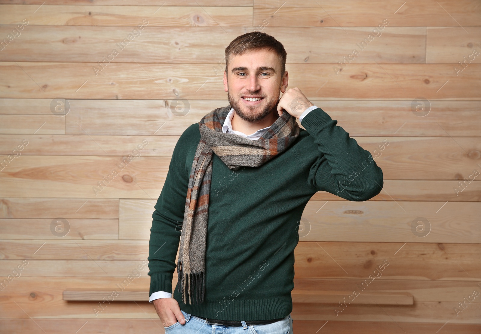 Photo of Handsome young man in warm sweater with scarf on wooden background