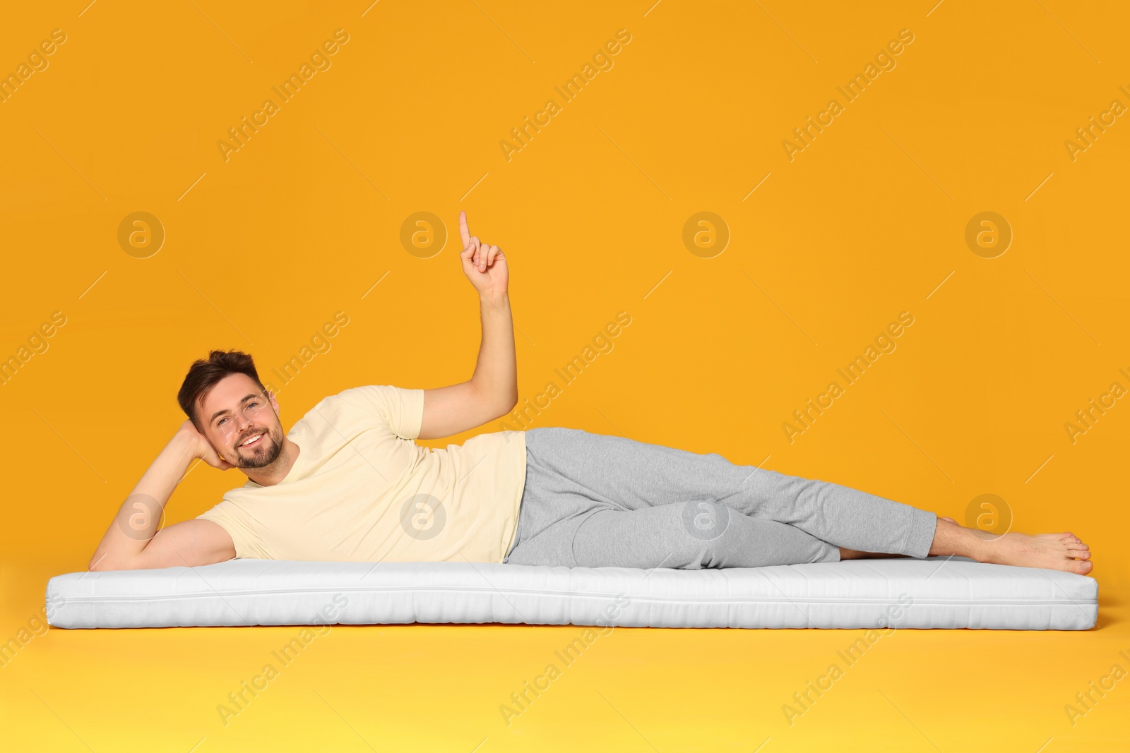 Photo of Man on soft mattress pointing upwards against orange background