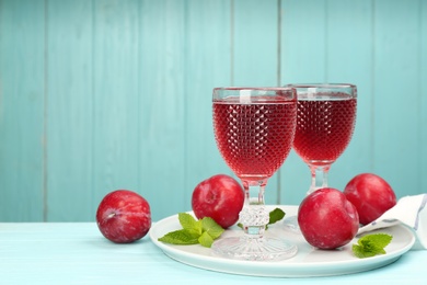 Photo of Delicious plum liquor, ripe fruits and mint on table against light blue background, space for text. Homemade strong alcoholic beverage