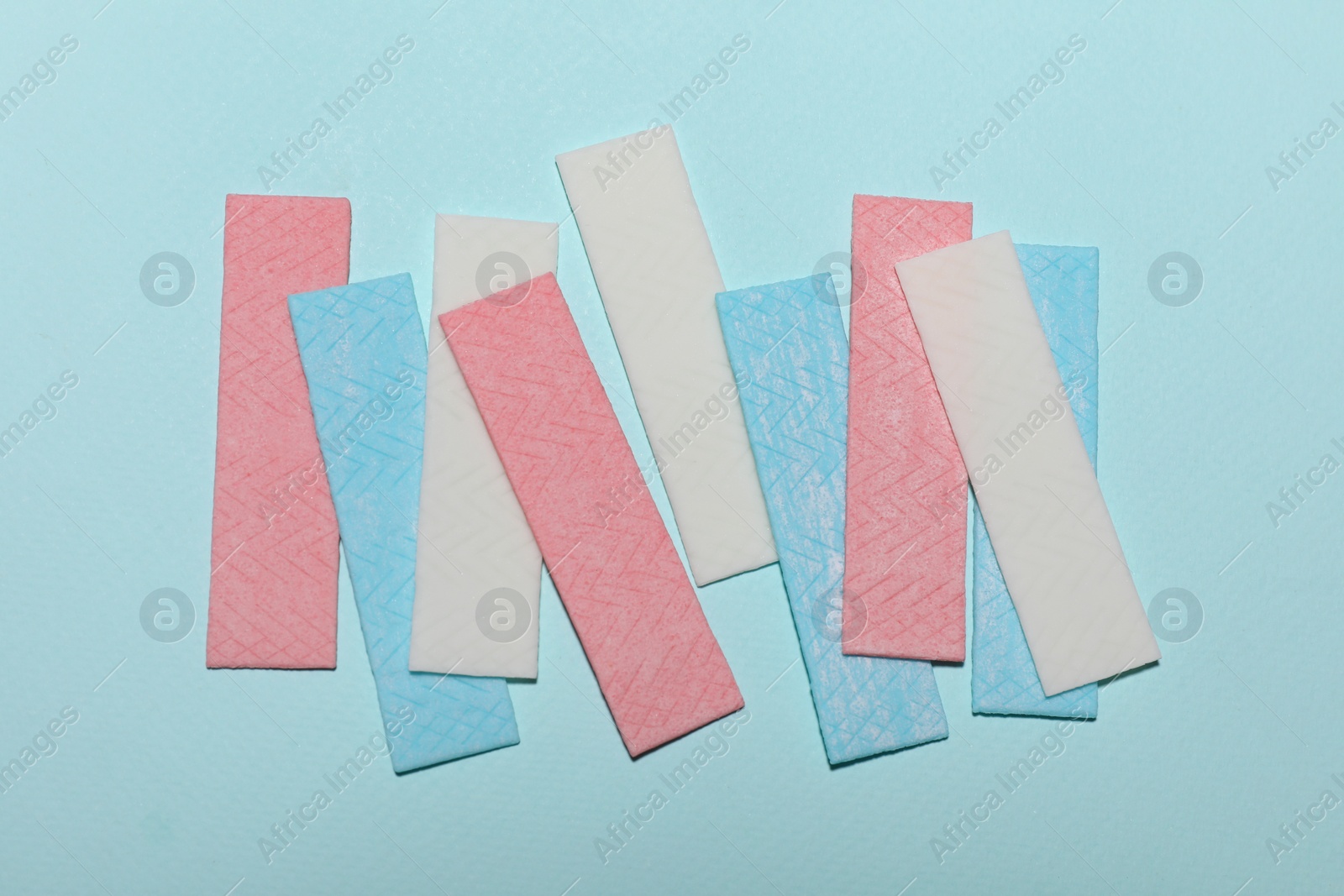 Photo of Sticks of tasty chewing gum on light blue background, flat lay