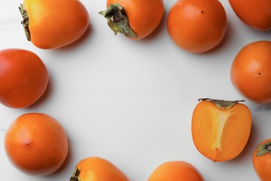 Delicious ripe persimmons on white table, flat lay. Space for text