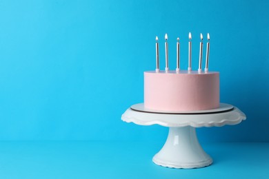 Photo of Birthday cake with burning candles on light blue background, space for text
