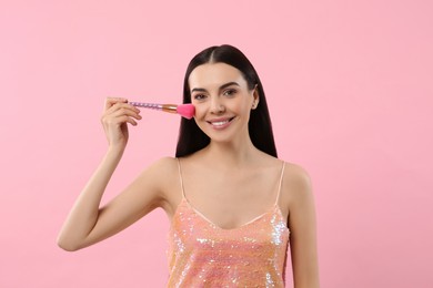 Photo of Beautiful woman applying makeup with brush on pink background