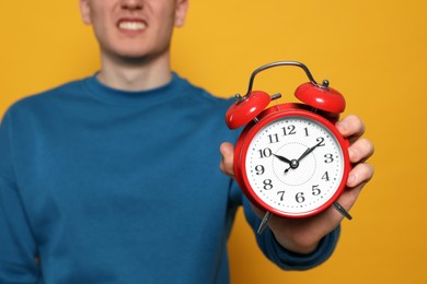 Photo of Young man with alarm clock on orange background, closeup. Being late concept