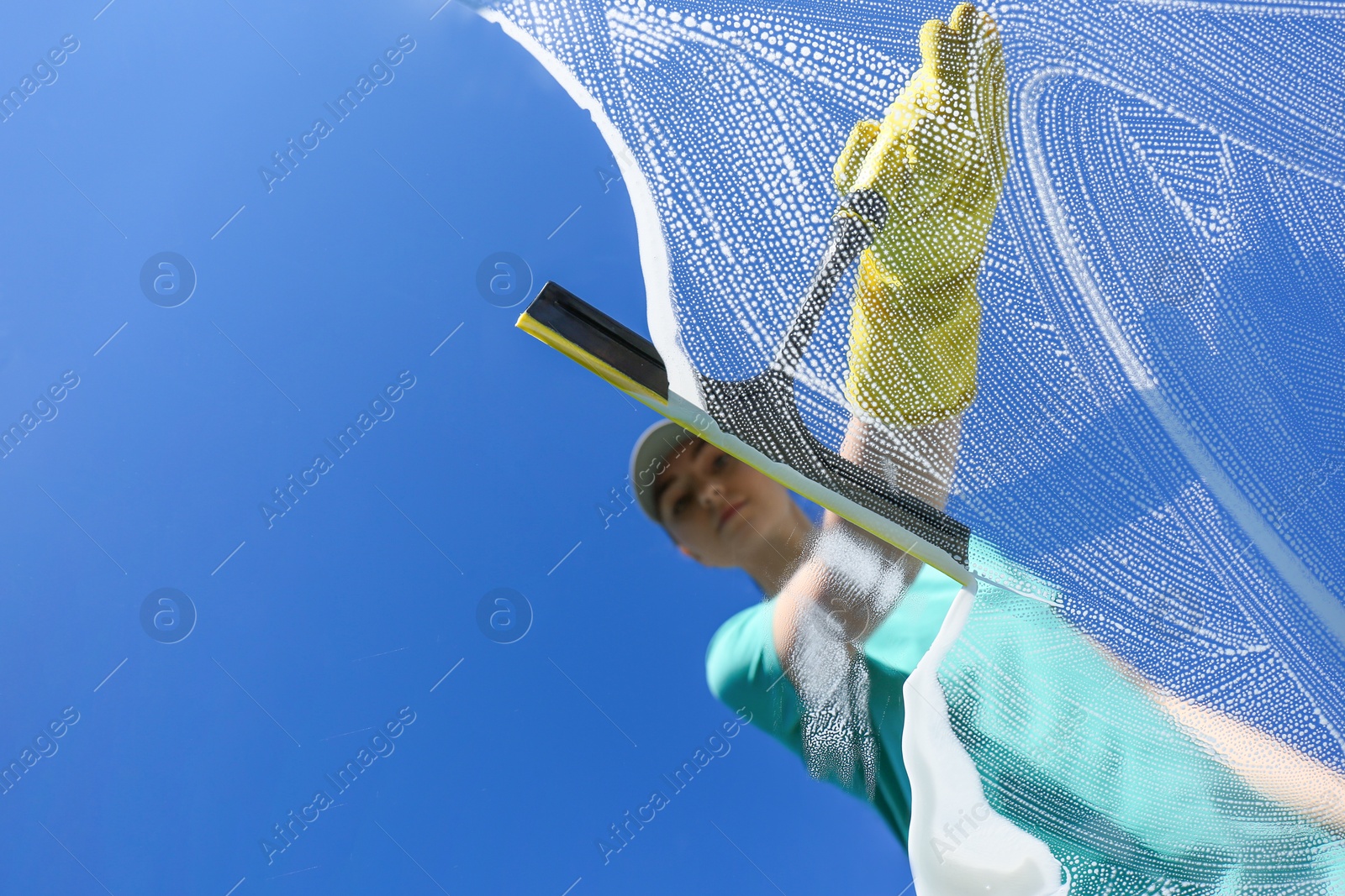 Photo of Woman cleaning glass with squeegee on sunny day