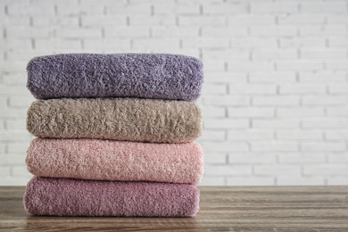 Photo of Stack of clean bath towels on wooden table near white brick wall. Space for text