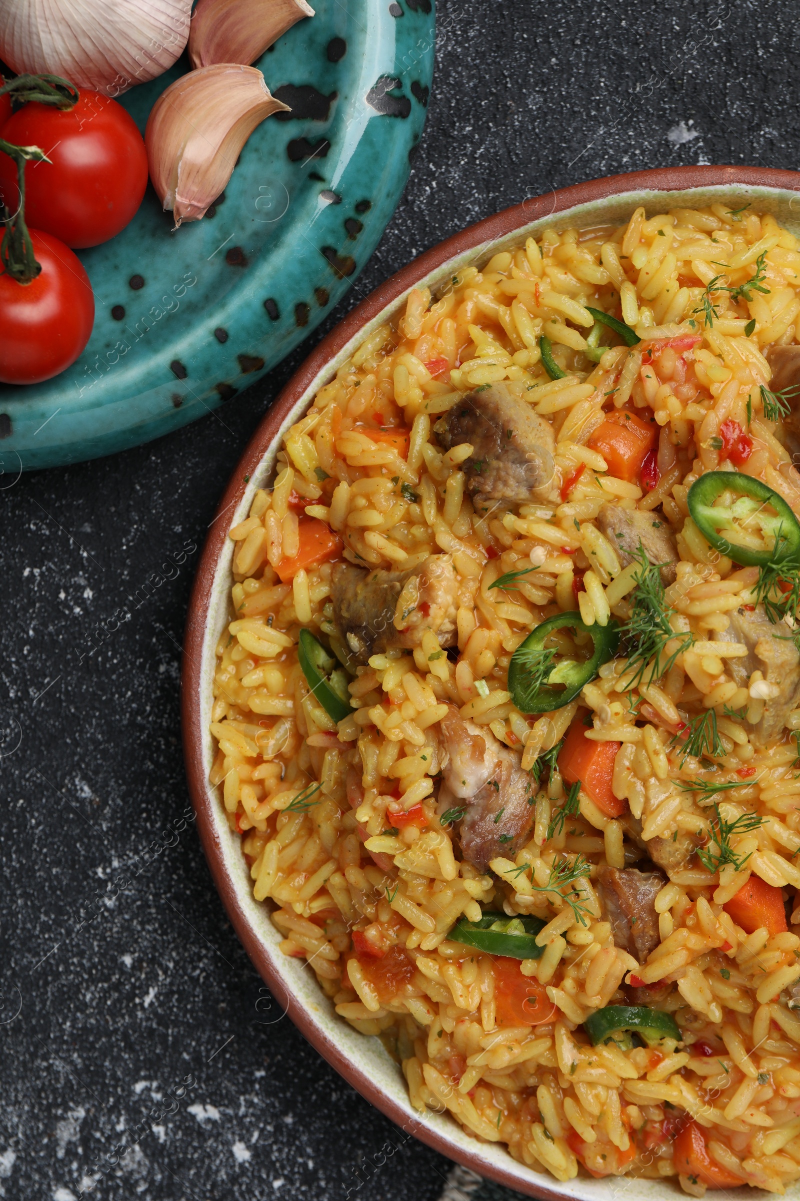 Photo of Delicious pilaf with meat and ingredients on black textured table, flat lay