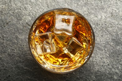 Photo of Whiskey and ice cubes in glass on grey textured table, top view