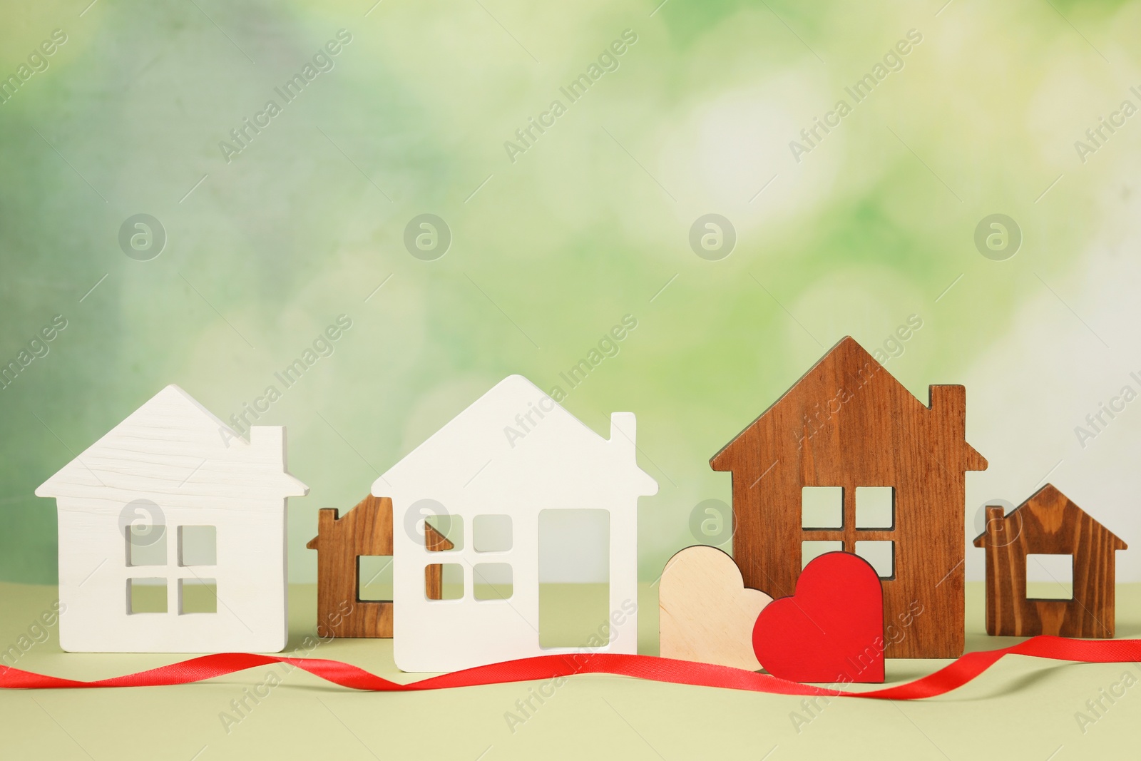 Photo of Long-distance relationship concept. House models, decorative hearts and red ribbon on light green background