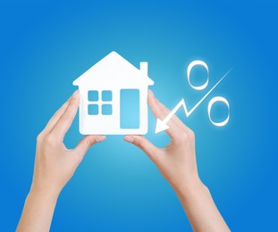 Mortgage concept. Woman holding house model on light blue background, closeup
