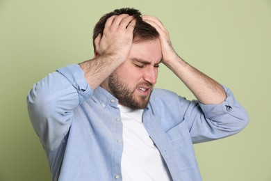 Man suffering from migraine on light green background