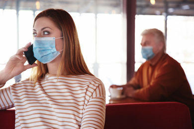 Woman with medical mask talking on mobile phone in cafe. Virus protection