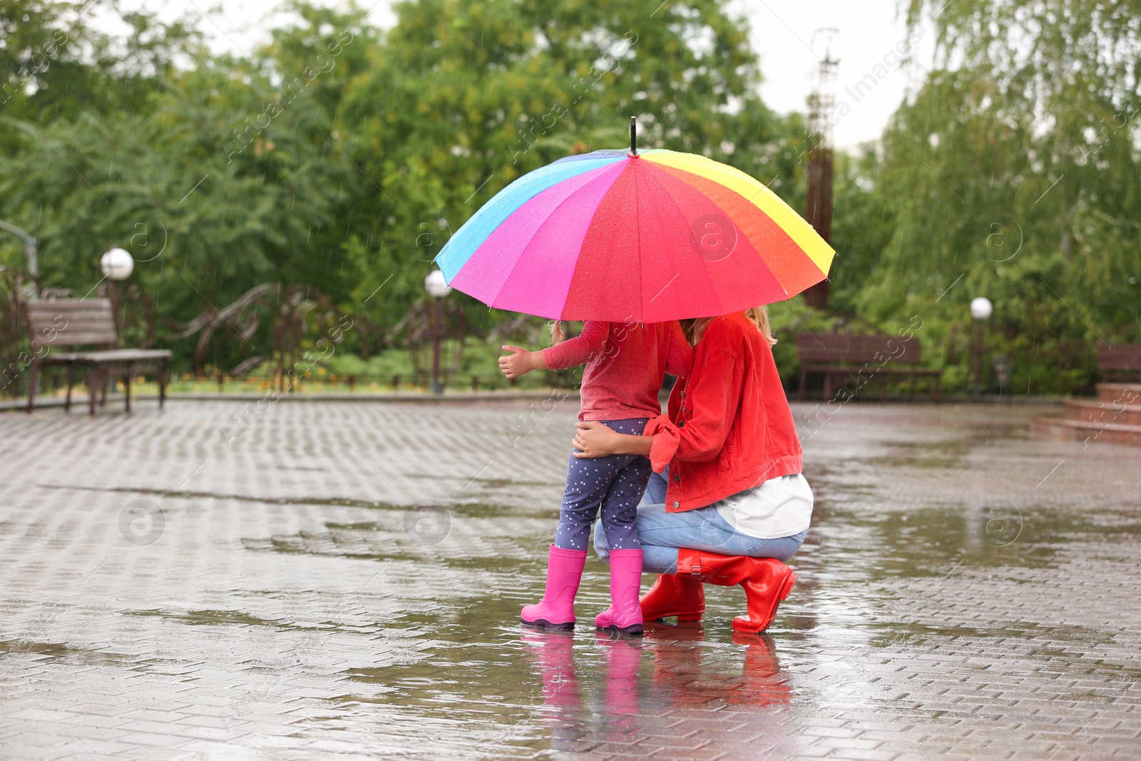 Photo of Mother and daughter with bright umbrella under rain outdoors