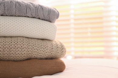 Stack of folded warm sweaters on bed indoors, closeup. Space for text