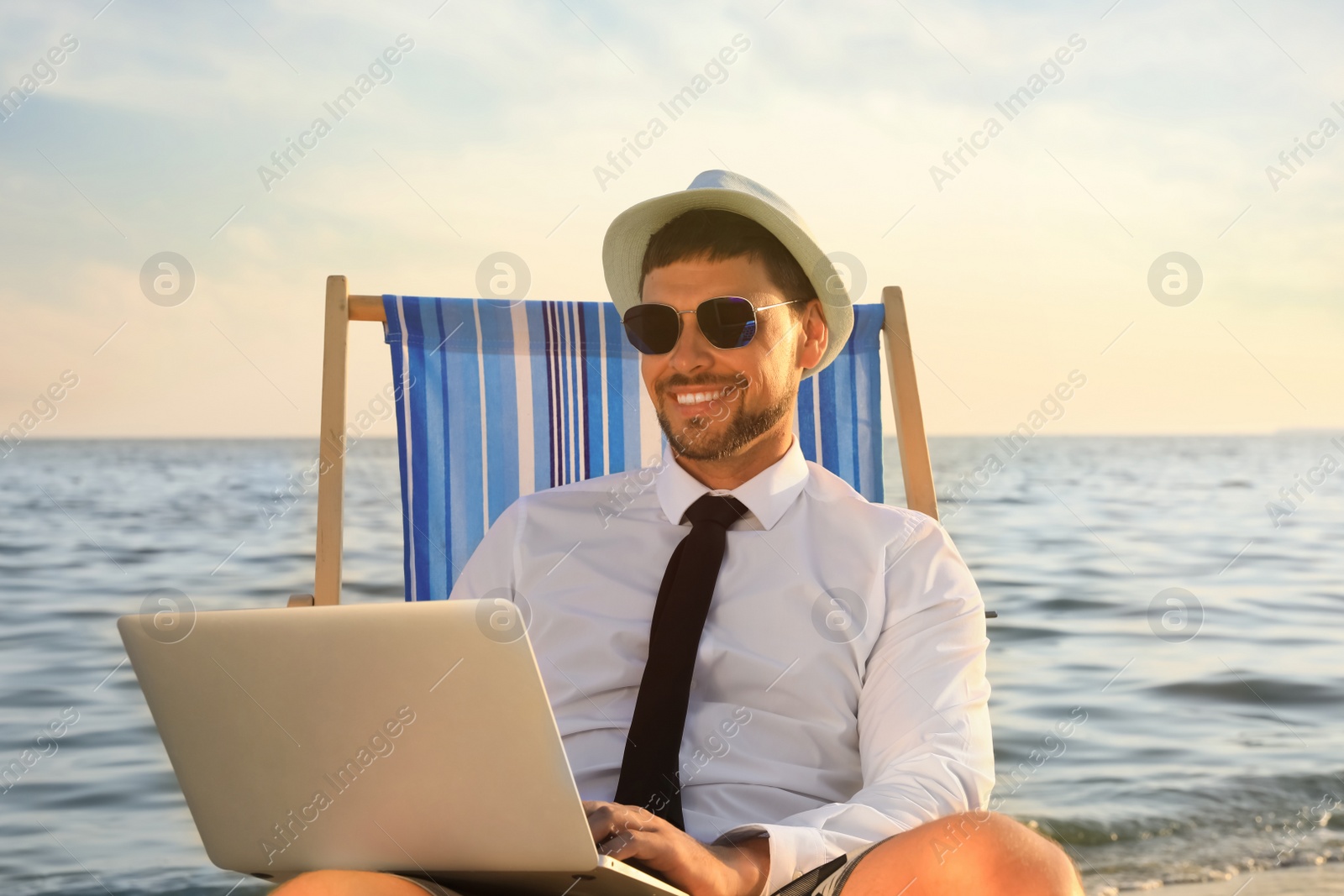 Photo of Happy man with laptop on deckchair near sea. Business trip