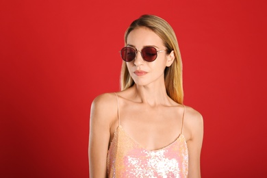 Photo of Beautiful woman in stylish sunglasses on red background