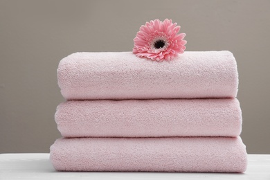 Photo of Stack of fresh towels with flower on table
