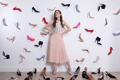Photo of Fashionable young woman surrounded by many different high heel shoes indoors