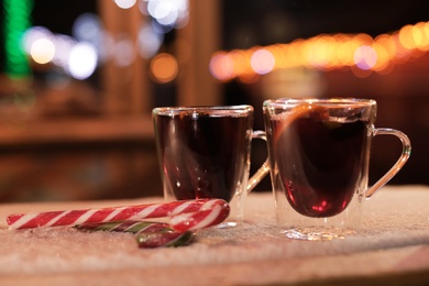 Photo of Glass cups of mulled wine and candy canes on table covered with snow outdoors. Space for text