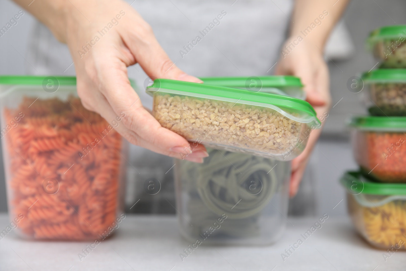 Photo of Woman with plastic container of raw couscous at light table, closeup. Food storage