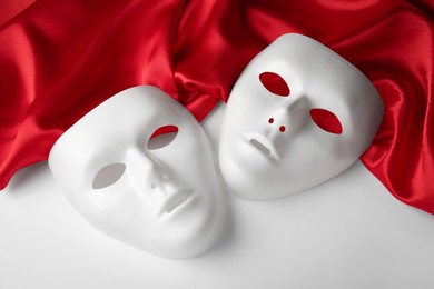 Theatre masks and red fabric on white background, above view