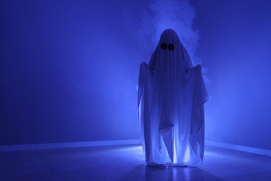 Creepy ghost. Woman covered with sheet in blue light, space for text