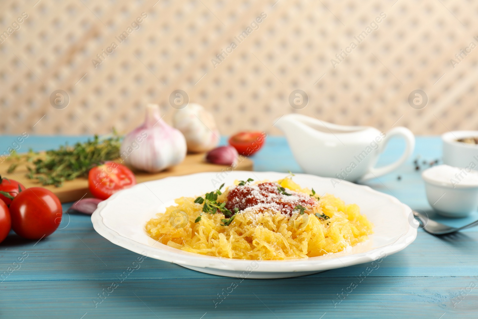 Photo of Tasty spaghetti squash with tomato sauce, cheese and thyme served on light blue wooden table