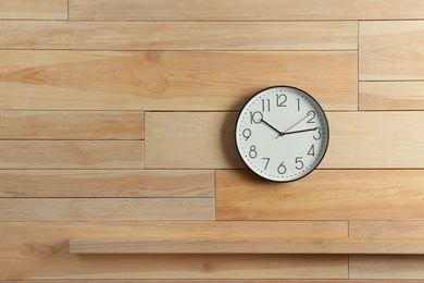 Photo of Stylish analog clock hanging on wooden wall. Space for text