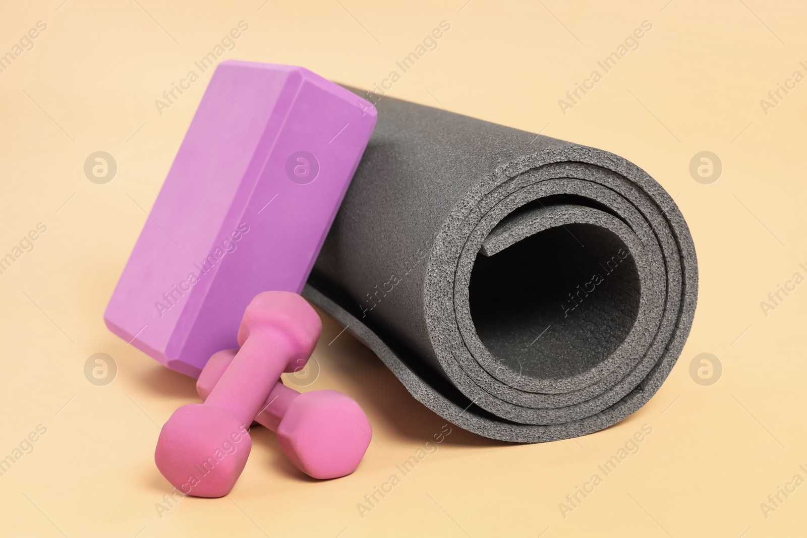 Photo of Grey exercise mat, yoga block and dumbbells on beige background
