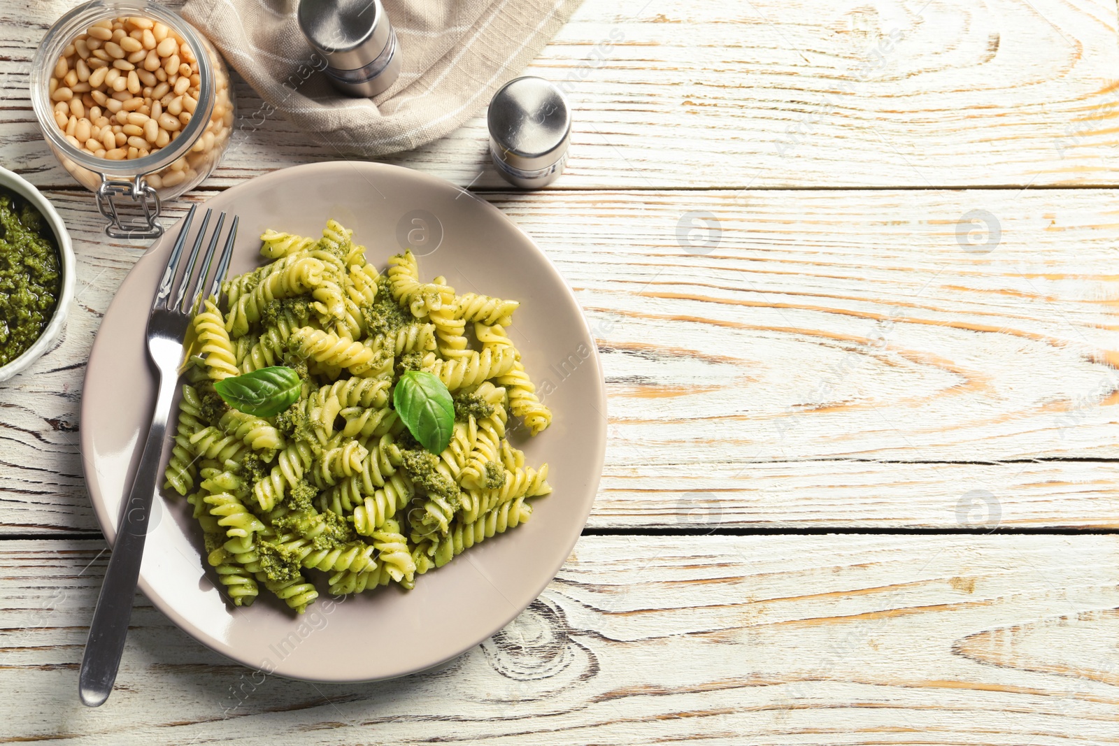 Photo of Flat lay composition with plate of delicious basil pesto pasta and space for text on wooden table