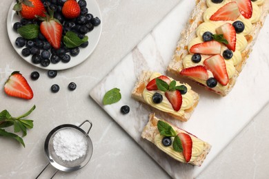 Tasty meringue roll with cream, strawberry, blueberry and mint on light grey marble table, flat lay