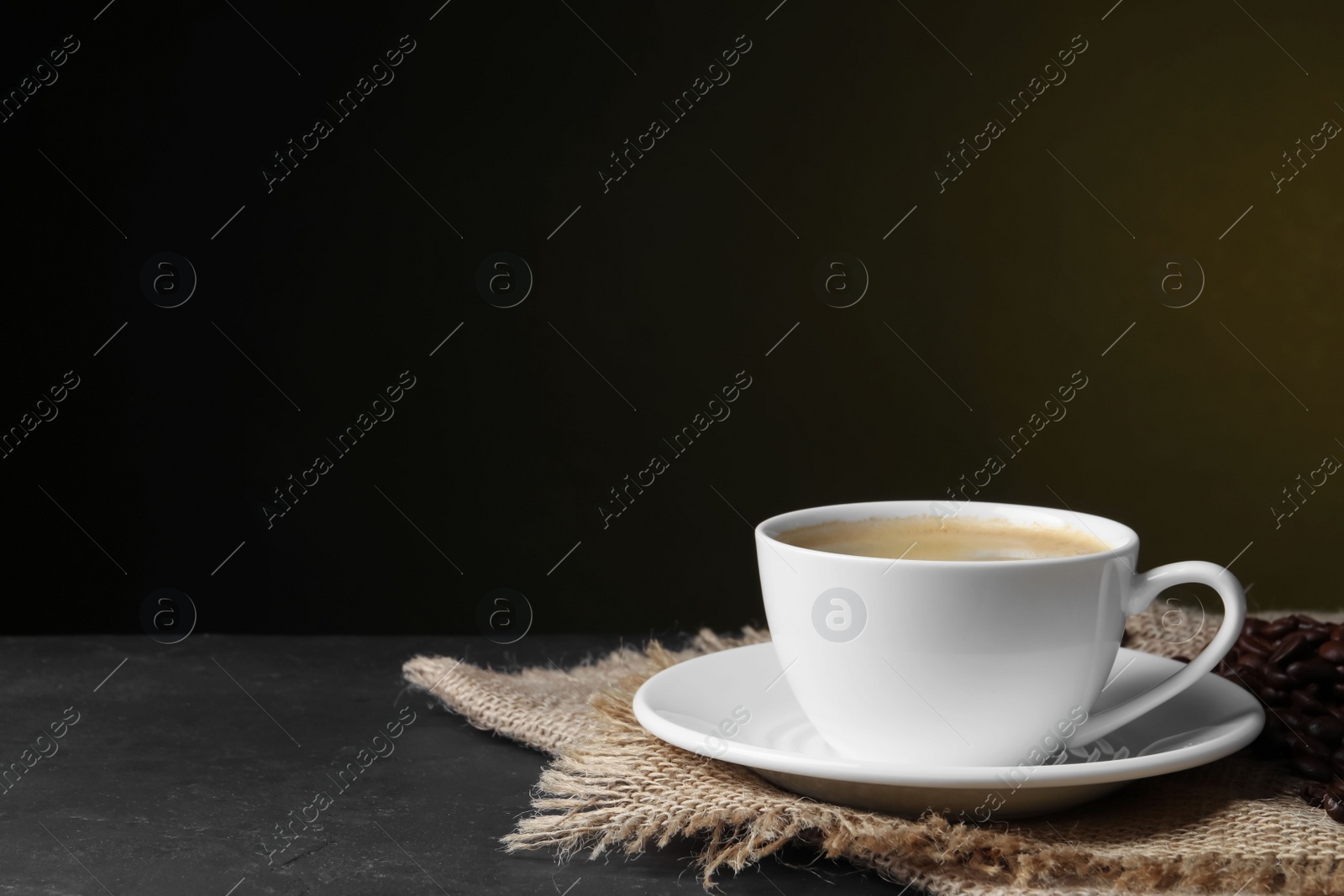 Photo of Cup of hot aromatic coffee and roasted beans on black table against dark background, space for text