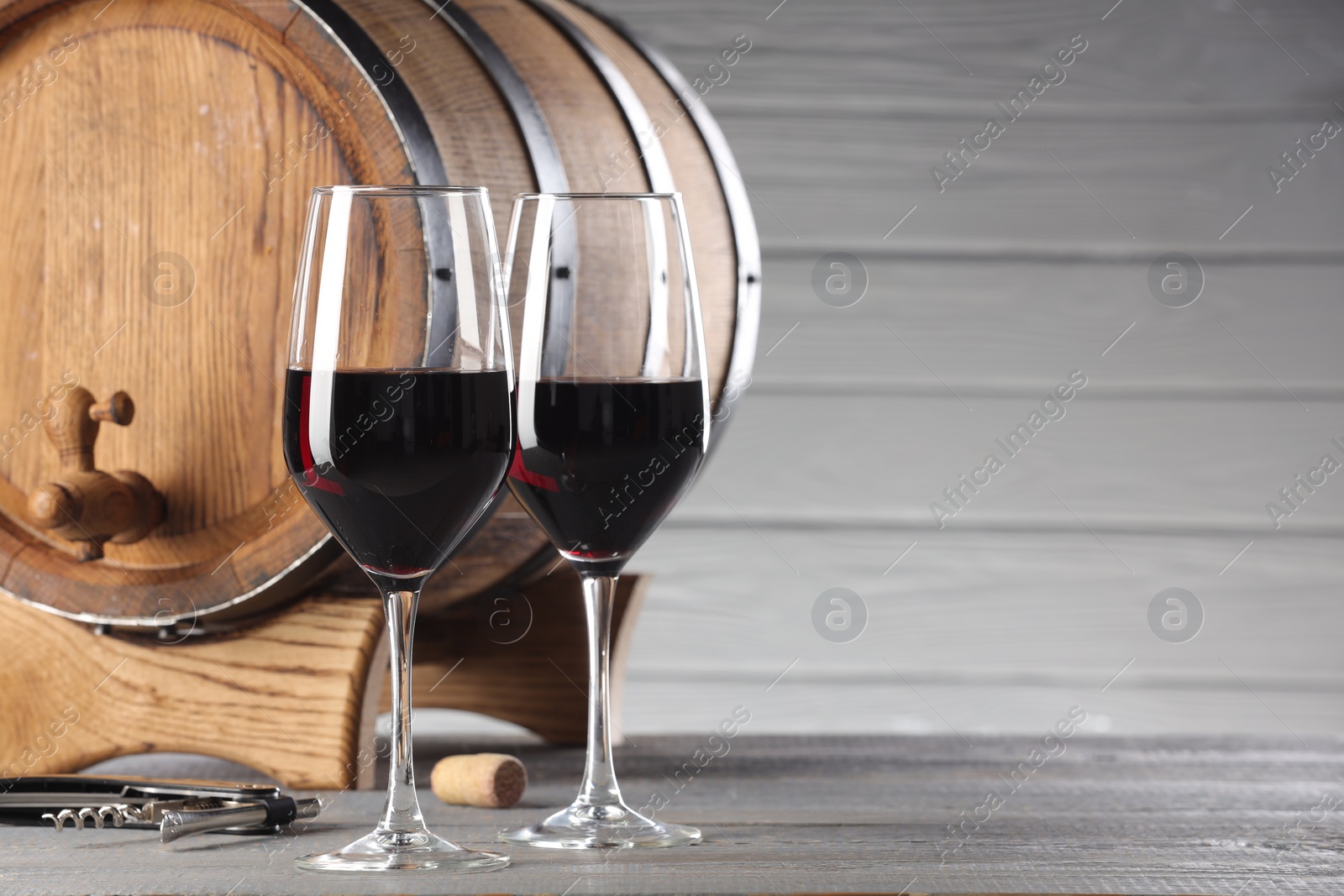 Photo of Glasses of delicious wine, wooden barrel and corkscrew on light grey table. Space for text