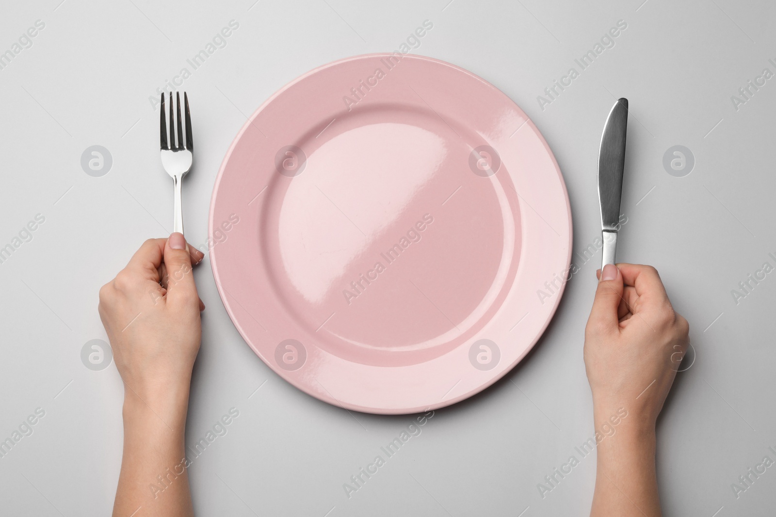 Photo of Woman with fork, knife and empty plate on grey background, top view