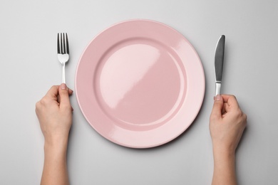 Woman with fork, knife and empty plate on grey background, top view