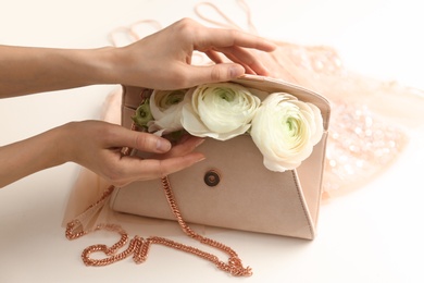 Woman holding stylish clutch bag with spring flowers on light background, closeup