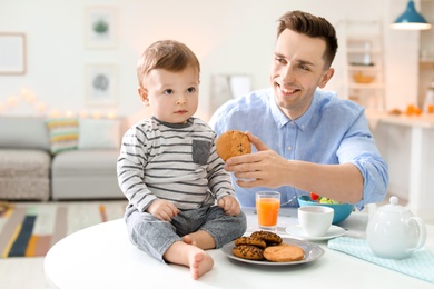 Photo of Young father with his cute little son eating in kitchen