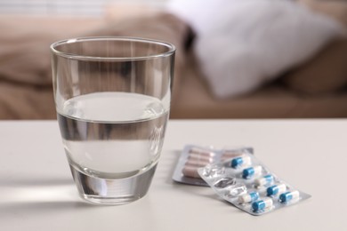 Photo of Glass of water and different pills in blisters on white table indoors, closeup. Space for text