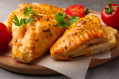 Photo of Fresh delicious puff pastry with cheese, tomatoes and parsley on grey table, closeup