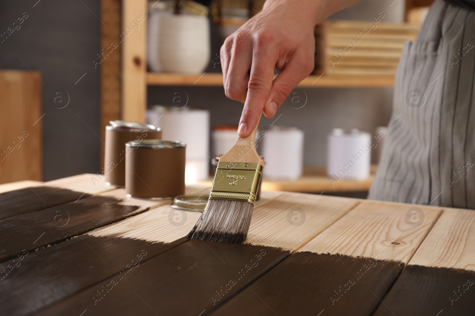 Photo of Man with brush applying wood stain onto wooden surface indoors, closeup