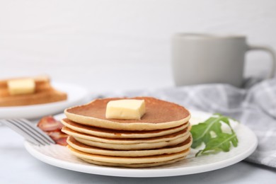 Tasty pancakes served with bacon and arugula on white table