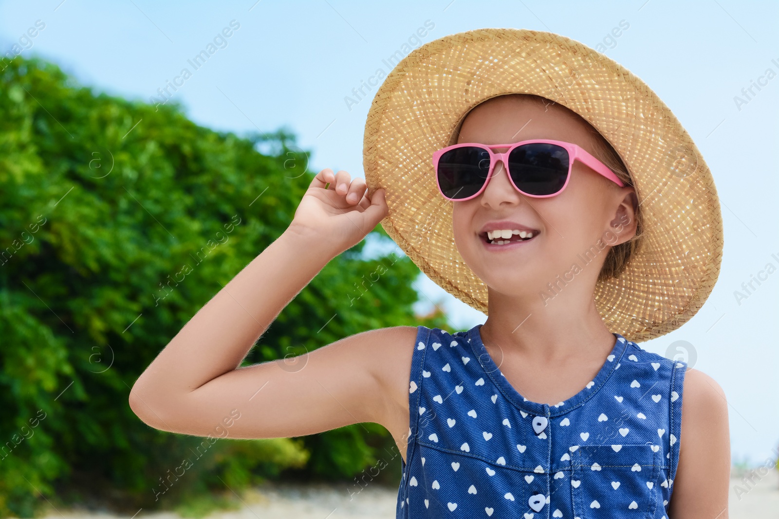 Photo of Little girl wearing sunglasses and hat at beach on sunny day