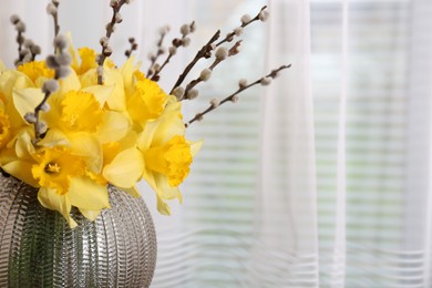 Bouquet of beautiful yellow daffodils and willow twigs in vase near window, closeup. Space for text