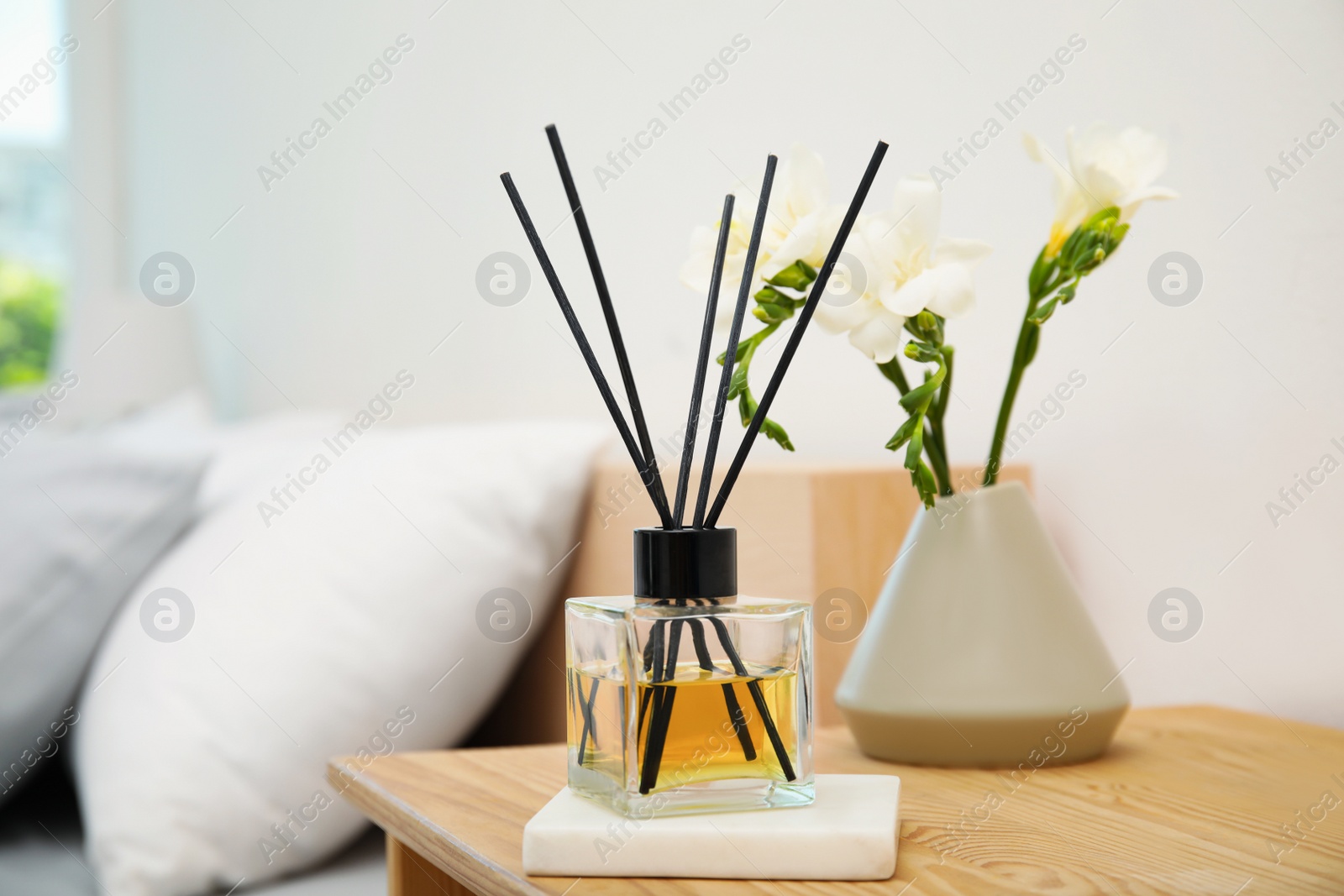 Photo of Reed diffuser and vase with bouquet on wooden nightstand in bedroom