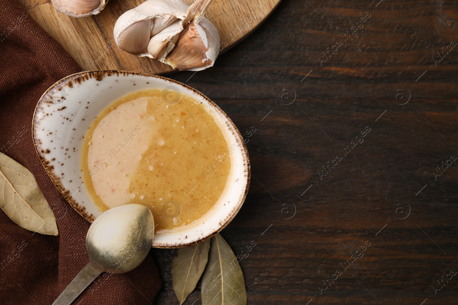 Photo of Delicious turkey gravy with bay leaves, garlic and spoon on wooden table, flat lay. Space for text