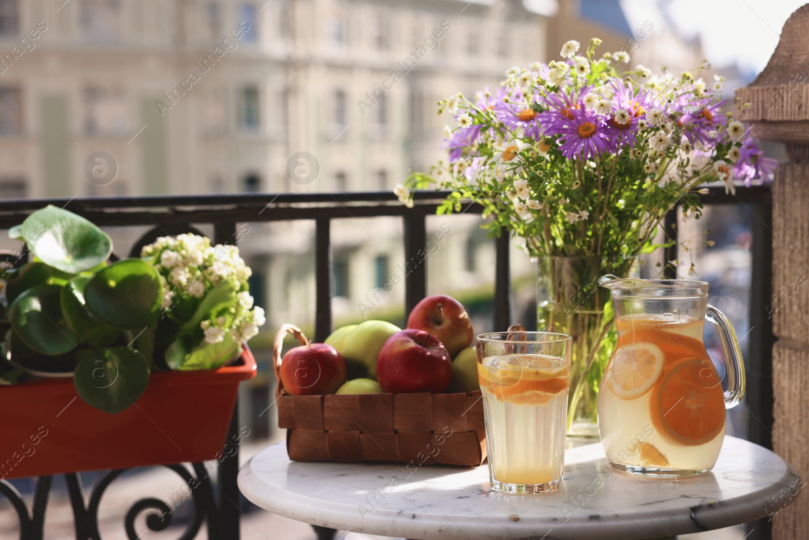 Photo of Relaxing atmosphere. Refreshing drink, apples and beautiful flowers on table near potted houseplant at balcony, space for text